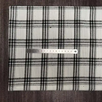 Une règle argentée de 15 cm repose sur une surface blanche recouverte de tissu en flanelle à carreaux colorés de Longon Craft France, un doux mélange de polyester et de coton parfait pour l'automne. L'arrière-plan est en bois foncé.