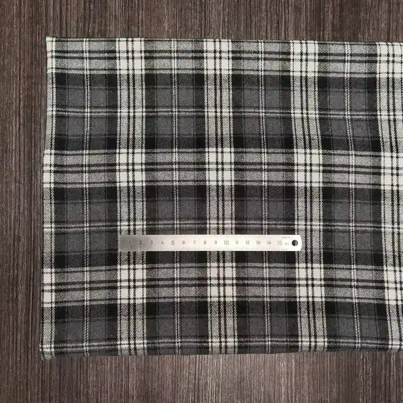Une pièce de Longon Craft France Tissu en flanelle à carreaux colorés au mètre, une matière ultra-douillette polyester-coton pour l'automne, repose sur du bois sombre, avec une règle métallique mesurant le tissu en centimètres.