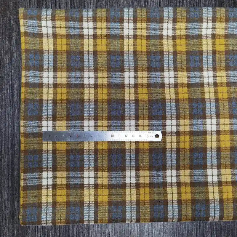 Un tissu en flanelle à carreaux colorés de Longon Craft France est étalé sur une surface grise, avec une règle métallique d'environ 20 cm posée dessus pour l'échelle.