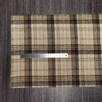 Une règle en métal est posée sur le tissu en flanelle à carreaux colorés au mètre de Longon Craft France, un tissu douillet en polyester-coton parfait pour l'automne, présenté sur une surface en bois sombre. La règle indique les mesures métriques.