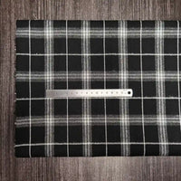 Une règle en métal repose sur le tissu en flanelle à carreaux colorés (polyester-coton) de Longon Craft France, une matière ultra-douillette pour l'automne, parfaite pour vêtements d'hiver, le tout sur une surface en bois sombre.