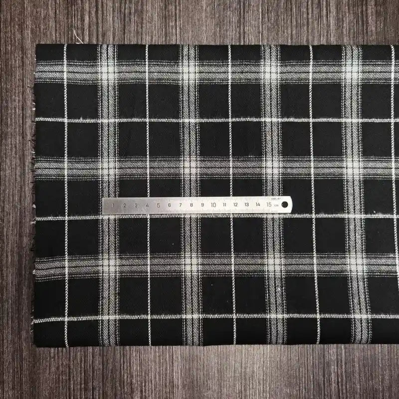 Une règle en métal repose sur le tissu en flanelle à carreaux colorés (polyester-coton) de Longon Craft France, une matière ultra-douillette pour l'automne, parfaite pour vêtements d'hiver, le tout sur une surface en bois sombre.