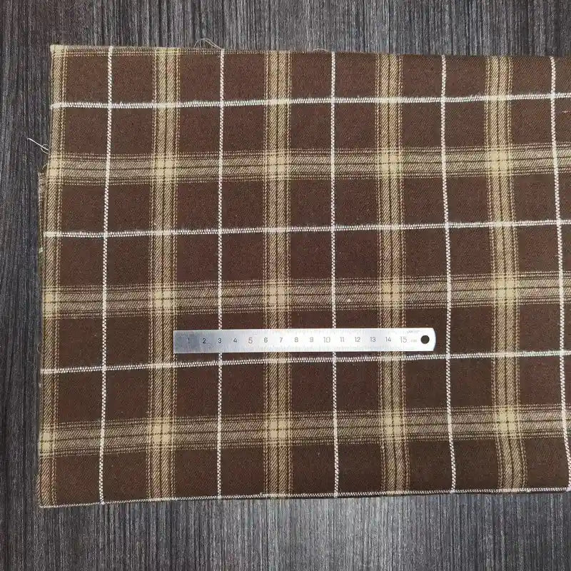A Tissu en flanelle à carreaux colorés Longon Craft France, polyester-coton ultra-douillet, est posé sur du bois sombre. Une règle métallique de 20 cm repose horizontalement sur cette matière confortable pour l'automne.