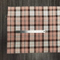 Un échantillon de Tissu en flanelle à carreaux colorés au mètre de Longon Craft France est présenté à plat sur une surface rayée grise, avec une règle métallique posée en travers pour l'échelle. Du polyester-coton ultra-douillet, parfait pour les projets d'automne.
