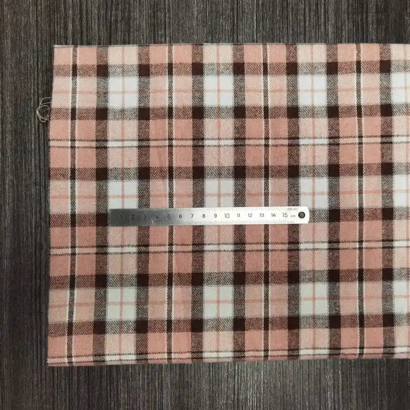 Un échantillon de Tissu en flanelle à carreaux colorés au mètre de Longon Craft France est présenté à plat sur une surface rayée grise, avec une règle métallique posée en travers pour l'échelle. Du polyester-coton ultra-douillet, parfait pour les projets d'automne.