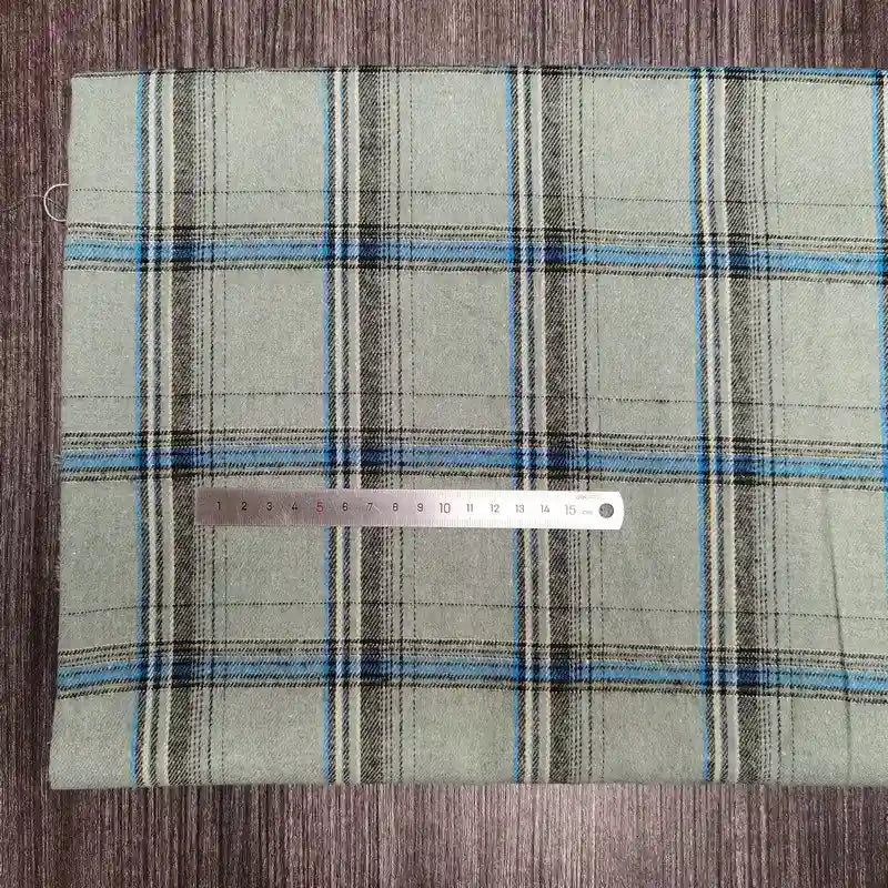 A piece of Tissu en flanelle à carreaux colorés Longon Craft France, doux polyester-coton pour l'automne, is posé à plat avec une règle métallique en centimètres sur le tissu pour indiquer l'échelle.