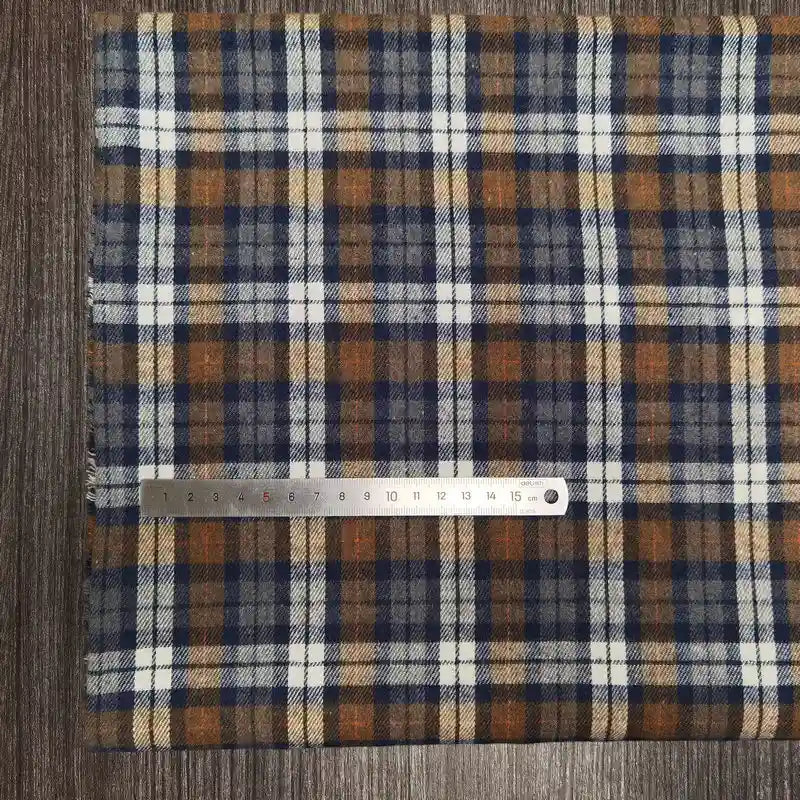 Une section du tissu en flanelle à carreaux colorés au mètre de Longon Craft France, une flanelle polyester-coton ultra-douillette pour l'automne, repose sur du bois avec une règle métallique affichant les centimètres.