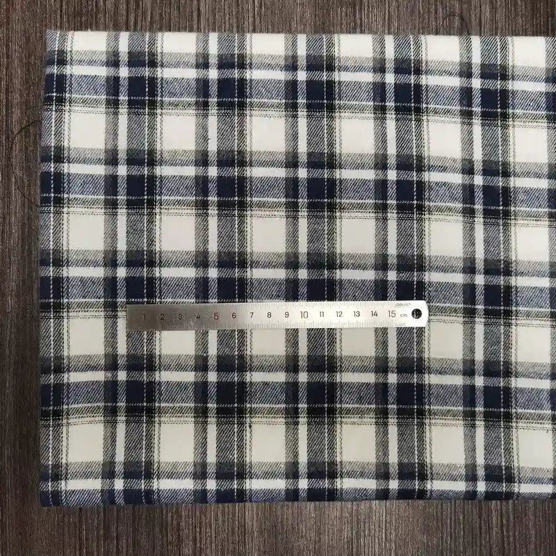 A piece of Tissu en flanelle à carreaux colorés Longon Craft France, une matière polyester-coton ultra-douillette, est posé sur une surface en bois. Un mètre ruban indique environ 15 cm sur le tissu confortable pour l'automne.