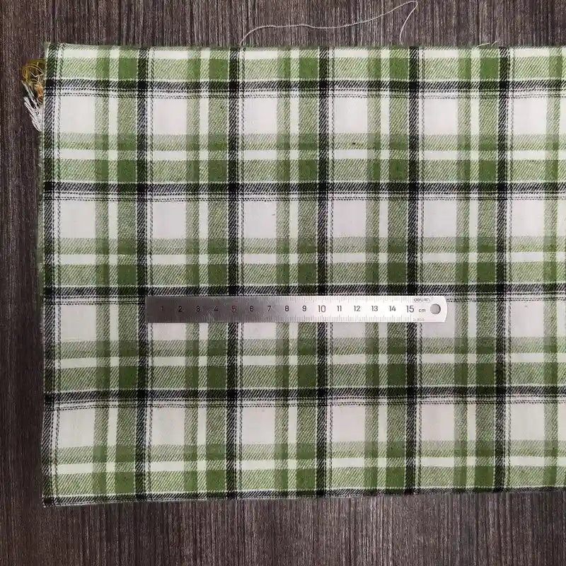 Un morceau de Tissu en flanelle à carreaux colorés au mètre de Longon Craft France, une flanelle polyester-coton ultra-douillette pour l'automne, repose sur une surface grise avec une règle argentée de 20 cm posée dessus.