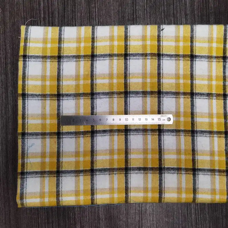 Une flanelle à carreaux jaune, blanche et noire de Longon Craft France est posée à plat sur du gris. Une règle métallique de 15 cm indique l'échelle de ce tissu en flanelle polyester-coton ultra-douillette, idéal pour vêtements d'automne et d'hiver.