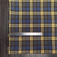 Un tissu en flanelle à carreaux colorés de Longon Craft France, idéal pour l'automne, est posé sur une surface en bois avec une règle métallique de 15 cm placée horizontalement le long du bord.