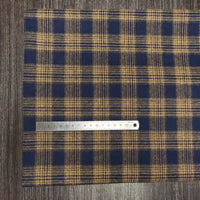 Un tissu en flanelle à carreaux colorés de Longon Craft France, ultra-douillet pour l'automne, est étalé sur une surface boisée avec une règle métallique de 20 cm posée dessus.