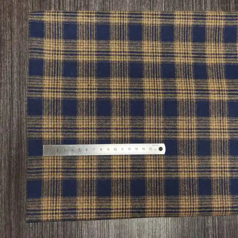 Un tissu en flanelle à carreaux colorés de Longon Craft France, ultra-douillet pour l'automne, est étalé sur une surface boisée avec une règle métallique de 20 cm posée dessus.