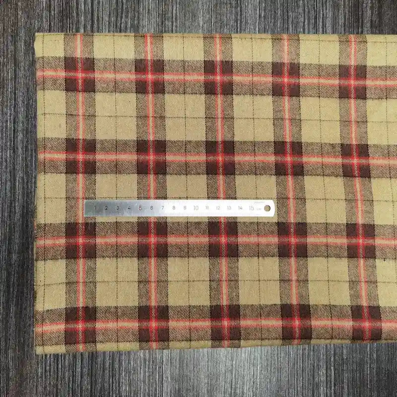 Une règle en métal repose sur le tissu en flanelle à carreaux colorés de Longon Craft France, une flanelle polyester-coton ultra-douillette vendue au mètre, idéale pour l'automne, posée sur une surface foncée à effet bois.