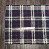 Une règle argentée repose sur un tissu en flanelle à carreaux coloré (Longon Craft France), polyester-coton ultra-doux au mètre, parfait pour les tissus d'ameublement d'automne. Le confortable tissu en flanelle à carreaux mesure environ 20 cm sous la règle.