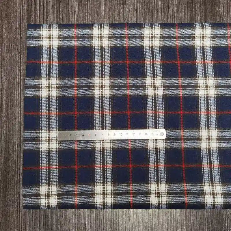 Une règle argentée repose sur un tissu en flanelle à carreaux coloré (Longon Craft France), polyester-coton ultra-doux au mètre, parfait pour les tissus d'ameublement d'automne. Le confortable tissu en flanelle à carreaux mesure environ 20 cm sous la règle.