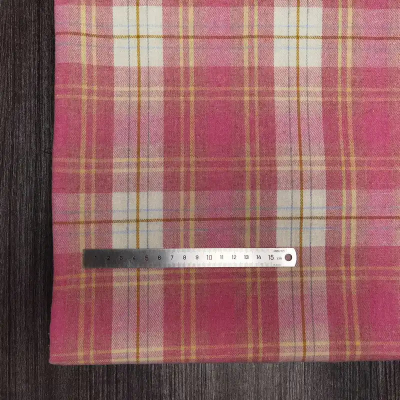 Une règle en métal repose sur le Tissu en flanelle à carreaux colorés au mètre de Longon Craft France, une flanelle polyester-coton ultra-douillette parfait pour l'automne, montrant ses couleurs rose, jaune et blanche sur une surface sombre.