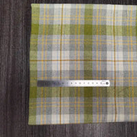 Une règle métallique de 15 cm repose sur un tissu en flanelle à carreaux verts, gris et blancs (Tissu en flanelle à carreaux colorés au mètre de Longon Craft France), en polyester-coton doux, présenté sur une surface grise texturée.