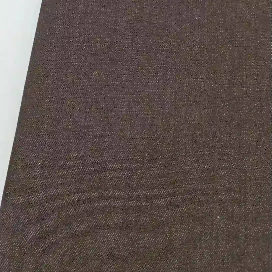 Gros plan sur le Tissu jean tissé coloré au mètre de Longan Craft France, un denim de coton de qualité supérieure de 6,5 oz sergé pour les jeans, montrant sa surface texturée brune avec un bord blanc sur la gauche.