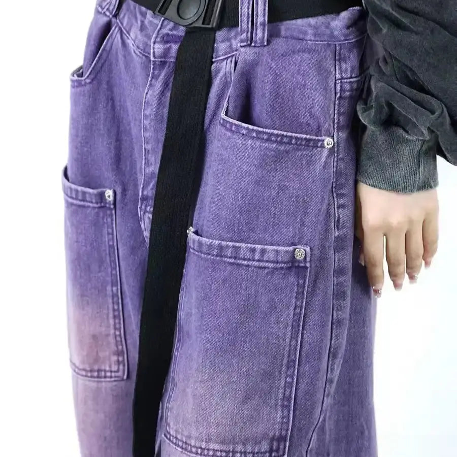 Une personne portant un pantalon à taille haute en tissu jean tissé coloré au mètre de Longan Craft France (6,5 oz cotton denim), avec de grandes poches sur le devant, une ceinture noire et un haut à manches longues gris foncé. Seuls le torse et une main sont visibles.