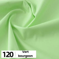 Un gros plan de la popeline de coton au mètre vert clair de Longan Craft France montre des plis doux et une texture lisse. L'étiquette "120 Vert bourgeon" est visible dans le coin inférieur gauche sur fond blanc.