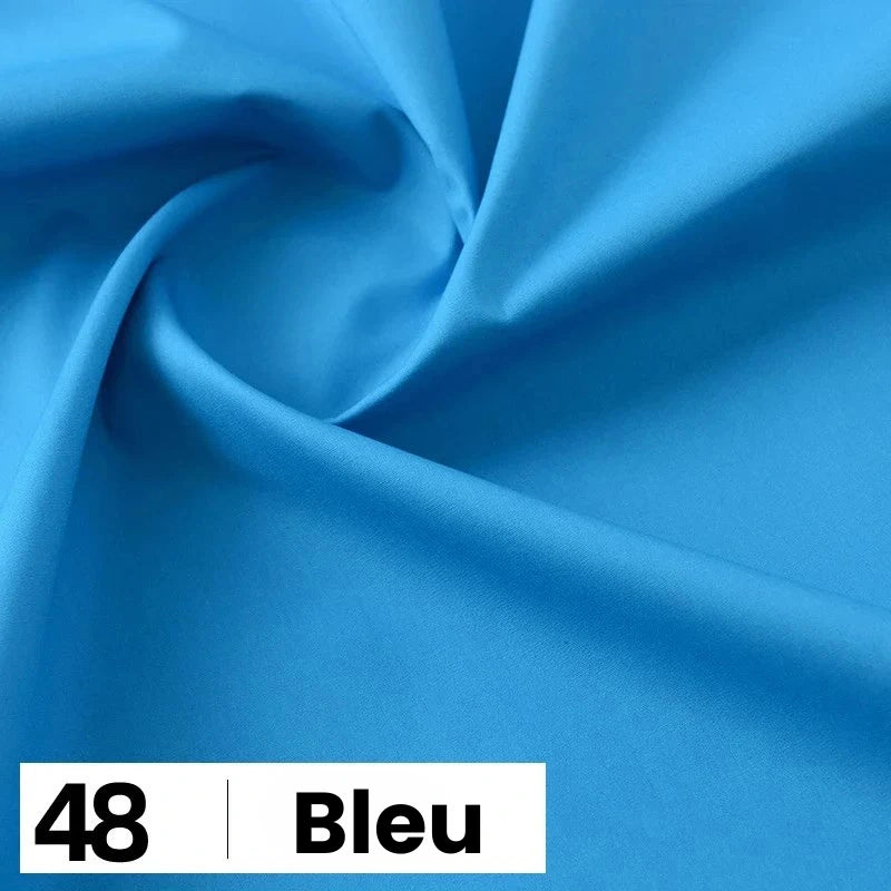 Gros plan sur la Popeline de coton au mètre de Longan Craft France, d'un bleu vif et lisse, légèrement tourbillonnante. Une étiquette blanche en bas indique "48 | Bleu" en texte noir. Parfait pour les chemises, les robes et les doublures.