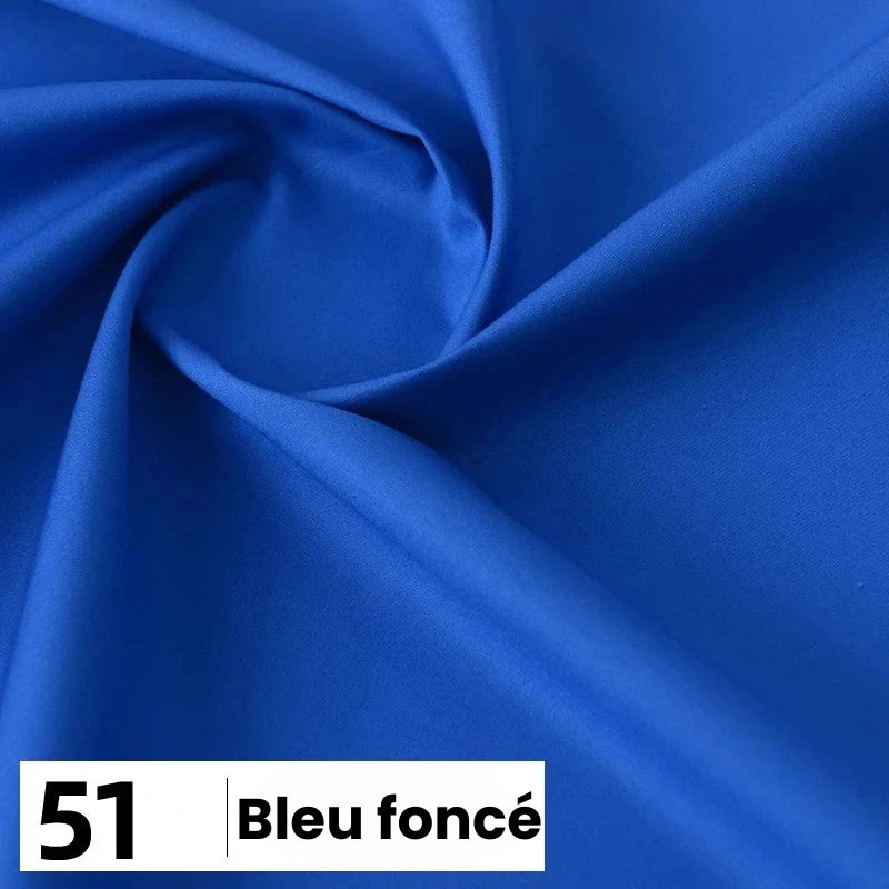 Un morceau de popeline de coton lisse et bleu foncé de Longan Craft France est drapé dans un tourbillon. Dans le coin, une étiquette indique "51 Bleu foncé". Idéal pour les chemises, les robes et les doublures, ce tissu de coton léger est vendu au mètre.