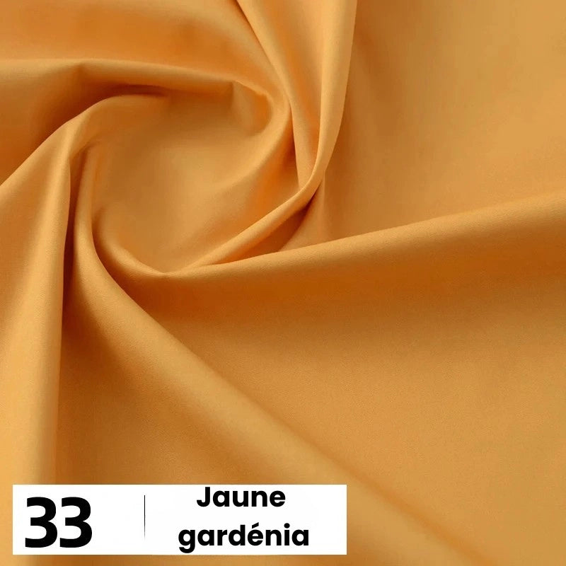 Un gros plan de la Popeline de coton au mètre jaune clair et lisse de Longan Craft France montre des plis doux. La mention "33 | Jaune gardénia" est inscrite en noir sur blanc en bas à gauche. Cette popeline de coton souple convient aux chemises, aux robes et aux doublures.