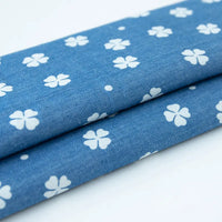 Deux pièces de Tissu denim coton imprimé de fleurs et d'étoiles de Longan Craft France sont empilées sur une surface blanche, montrant les motifs floraux et étoilés répétitifs du denim imprimé.