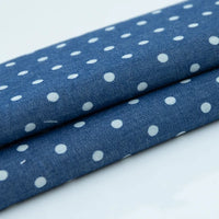 Gros plan sur deux pièces pliées de Tissu denim coton imprimé de fleurs et d'étoiles au mètre de Longan Craft France, un tissu denim imprimé léger présenté sur une surface unie.
