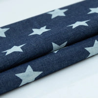 Tissu denim coton imprimé de fleurs et d'étoiles au mètre de Longan Craft France, en denim léger, présente un motif d'étoiles blanches sur fond bleu. Le tissu est soigneusement plié pour mettre en valeur le design répétitif.