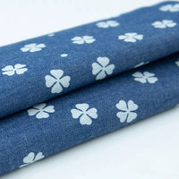 Deux pièces de Tissu denim coton imprimé de fleurs et d'étoiles au mètre de Longan Craft France sont soigneusement pliées, mettant en valeur la texture et le motif imprimé de ce denim léger idéal pour les vêtements.