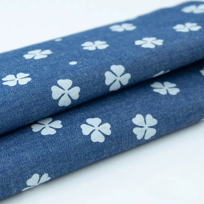Deux pièces de Tissu denim coton imprimé de fleurs et d'étoiles au mètre de Longan Craft France sont soigneusement pliées, mettant en valeur la texture et le motif imprimé de ce denim léger idéal pour les vêtements.