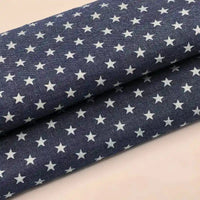 Le Tissu denim coton imprimé de fleurs et d'étoiles au mètre de Longan Craft France est un denim léger bleu foncé orné d'étoiles blanches, présenté sur une surface claire.