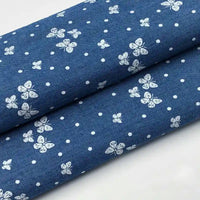 Gros plan sur Tissu denim coton imprimé de fleurs et d'étoiles au mètre de Longan Craft France, montrant le denim léger plié avec un délicat imprimé floral et étoilé du dessin continu.