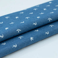Gros plan sur le denim bleu plié coton imprimé de fleurs et d'étoiles par Longan Craft France, montrant son motif délicat - parfait tissu denim léger au mètre pour vêtements.