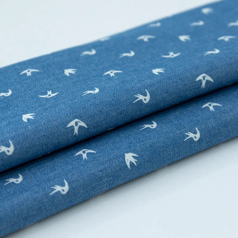 Gros plan sur le denim bleu plié coton imprimé de fleurs et d'étoiles par Longan Craft France, montrant son motif délicat - parfait tissu denim léger au mètre pour vêtements.