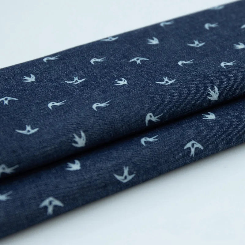 Tissu denim coton léger de Longan Craft France, imprimé au mètre avec motifs de fleurs et d'étoiles blanches sur fond bleu foncé. Idéal pour vêtements, tissu doux à motif régulier et distribution homogène.