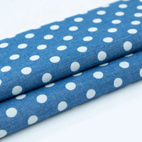 Gros plan sur deux pièces pliées de Tissu denim coton imprimé de fleurs et d'étoiles au mètre par Longan Craft France, montrant le tissu denim imprimé clair sur un fond uni.