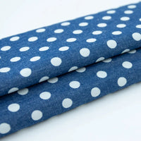 Gros plan sur deux pièces pliées de Tissu denim coton imprimé de fleurs et d'étoiles au mètre de Longan Craft France, un denim léger parfait pour vêtements, superposé sur une surface blanche.