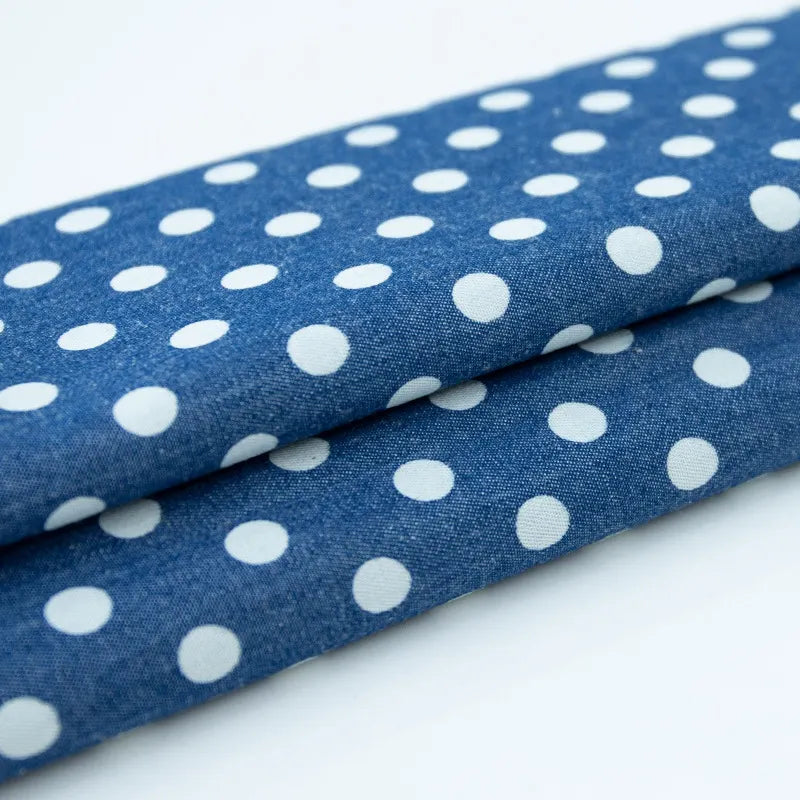 Gros plan sur deux pièces pliées de Tissu denim coton imprimé de fleurs et d'étoiles au mètre de Longan Craft France, un denim léger parfait pour vêtements, superposé sur une surface blanche.