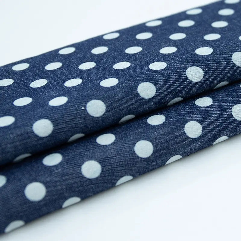 Gros plan sur le pliage de Tissu denim coton imprimé de fleurs et d'étoiles au mètre par Longan Craft France. Ce tissu denim imprimé, lisse et léger, se pose à plat sur un fond blanc et est idéal pour les vêtements.