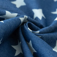 Gros plan sur le tissu denim coton imprimé de fleurs et d'étoiles au mètre de Longan Craft France, montrant le tissu denim léger avec des motifs d'étoiles blanches délicatement pliés au centre.