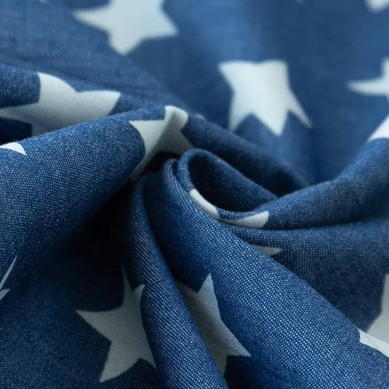 Gros plan sur le tissu denim coton imprimé de fleurs et d'étoiles au mètre de Longan Craft France, montrant le tissu denim léger avec des motifs d'étoiles blanches délicatement pliés au centre.