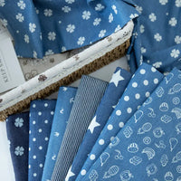 Une sélection de tissu denim coton imprimé de fleurs et d'étoiles au mètre de Longan Craft France est disposée en éventail dans un panier doublé de tissu imprimé - idéal denim imprimé pour les vêtements.