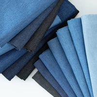 Plusieurs échantillons pliés de Tissu denim délavé 6 oz de Longan Craft France, dans des tons de bleu et de noir, sont disposés en deux motifs en éventail sur une surface blanche. Ce tissu denim de coton doux est idéal pour les jeans et est disponible au mètre.