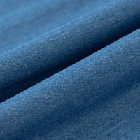 Gros plan sur le Tissu denim délavé 6 oz au mètre de Longan Craft France, un denim de coton doux de couleur bleue dont le tissage fin et les plis délicats révèlent une texture lisse et des ombres subtiles.