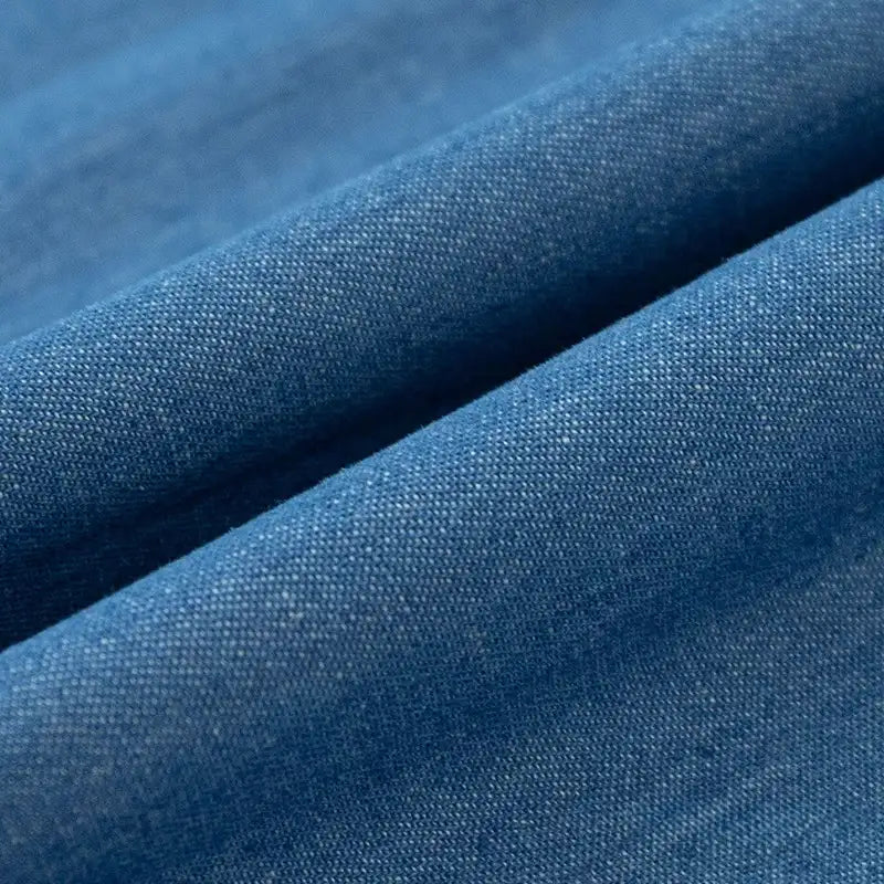 Gros plan sur le Tissu denim délavé 6 oz au mètre de Longan Craft France, un denim de coton doux de couleur bleue dont le tissage fin et les plis délicats révèlent une texture lisse et des ombres subtiles.