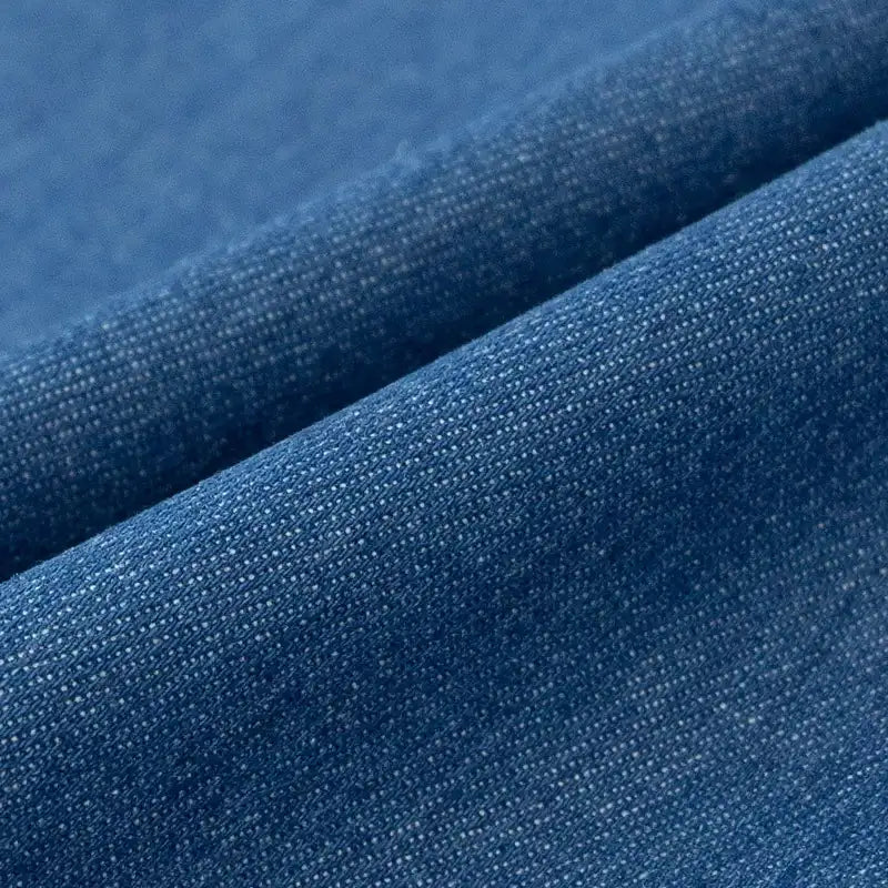 Gros plan sur le Tissu denim délavé 6 oz au mètre de Longan Craft France, un tissu de coton bleu doux avec un tissage visible, de subtiles variations de couleur et de légers plis qui créent des lignes diagonales à travers la texture.