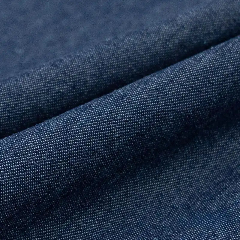 Gros plan sur le Tissu denim délavé 6 oz au mètre de Longan Craft France, montrant la texture tissée et les fils fins du tissu de coton bleu doux. Le tissu légèrement plié crée un pli visible sur l'image.